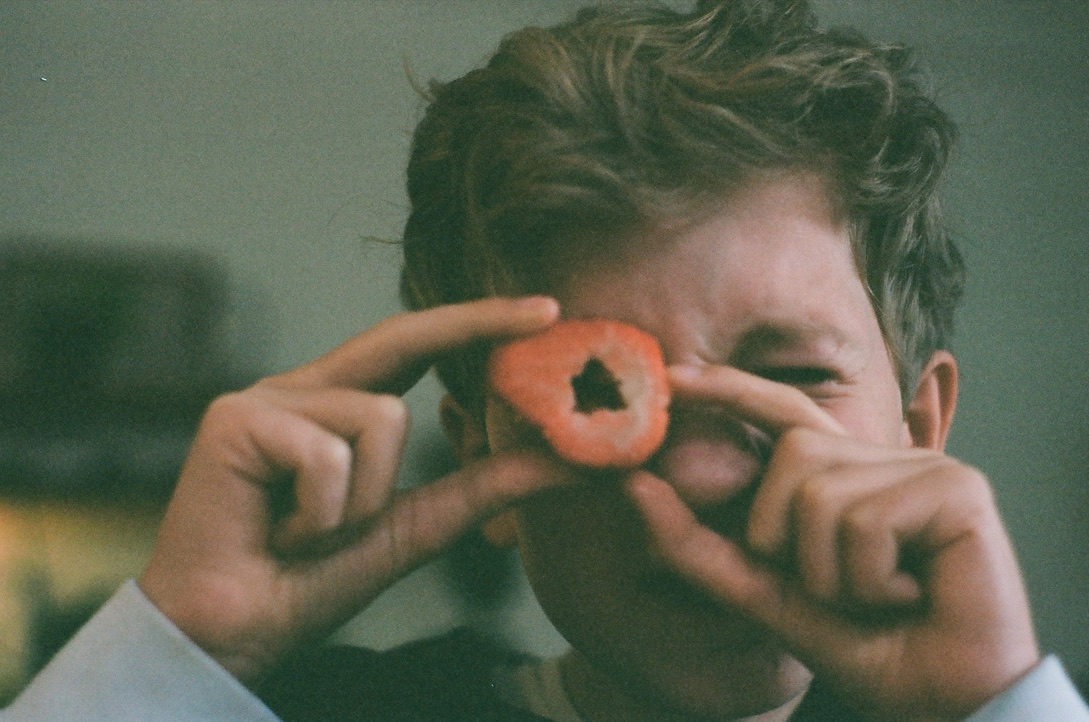 A kid holding up a strawberry to measure it